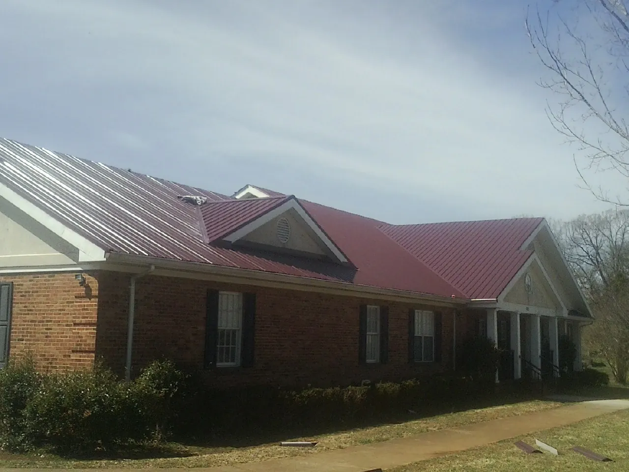 Red metal roof with gabled entries on a long brick building, from a Hail Damage Roof Repair job in Tamworth