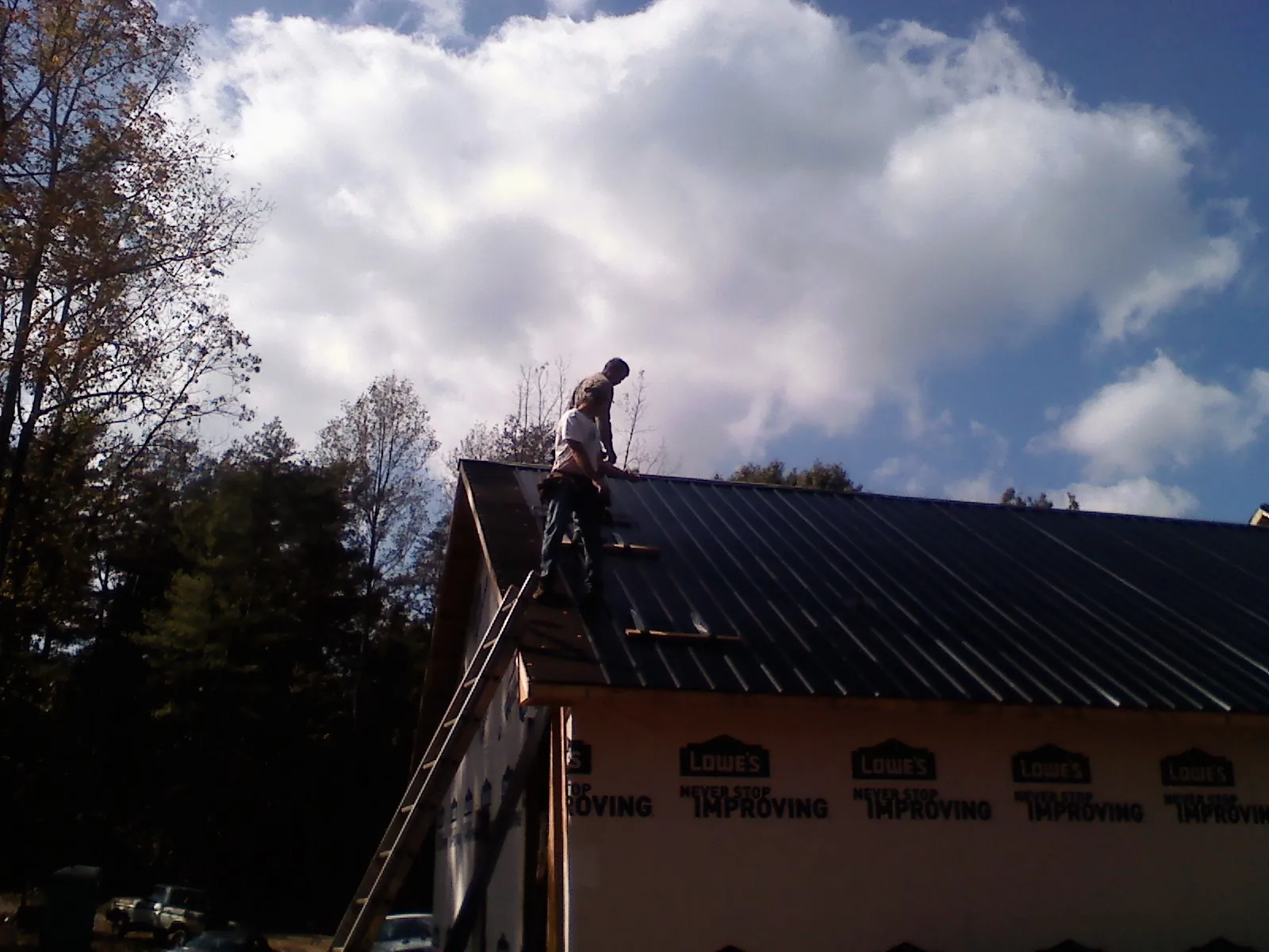 Roofer fastening dark metal panels high against a cloudy sky, from a Roof Inspection job in Tamworth