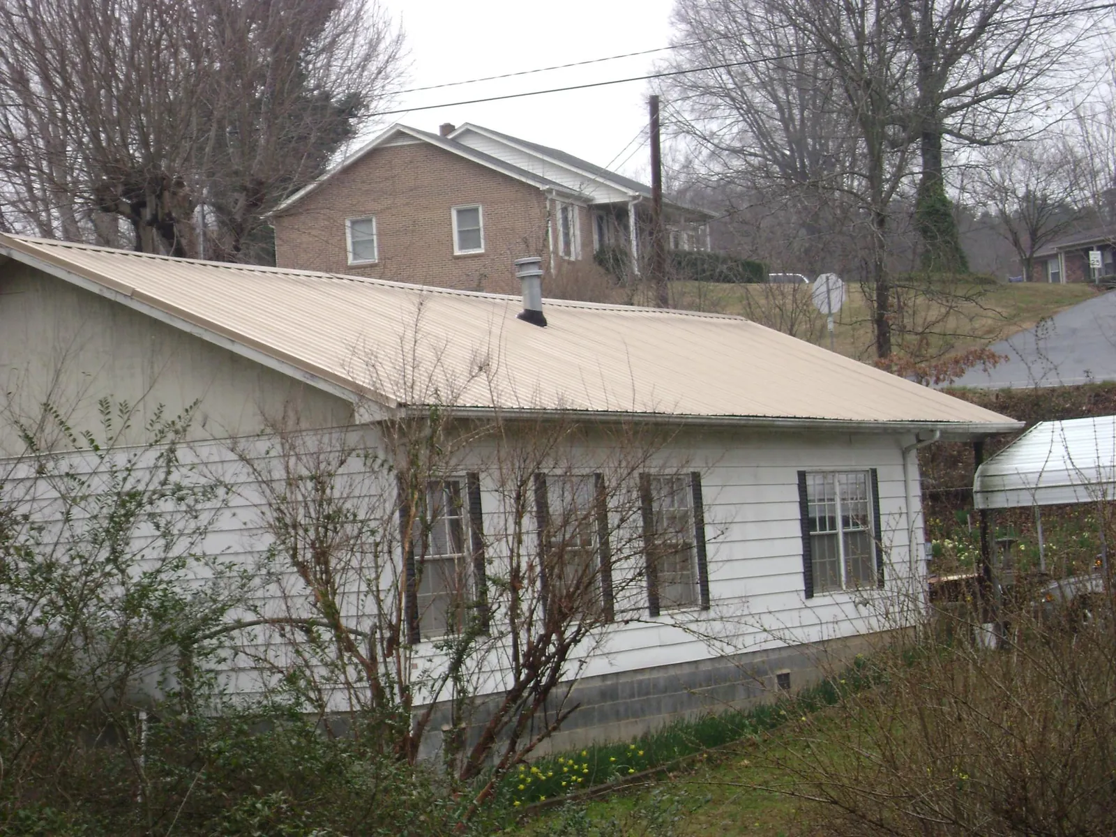 Tan metal roof on a white sided house set into a hillside — Commercial Roofing by Roofing Brothers in Tamworth