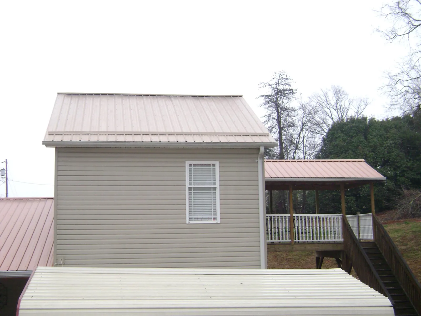 Tan metal roofs on a two story addition and attached porch, from a Roof Replacement job in Tamworth
